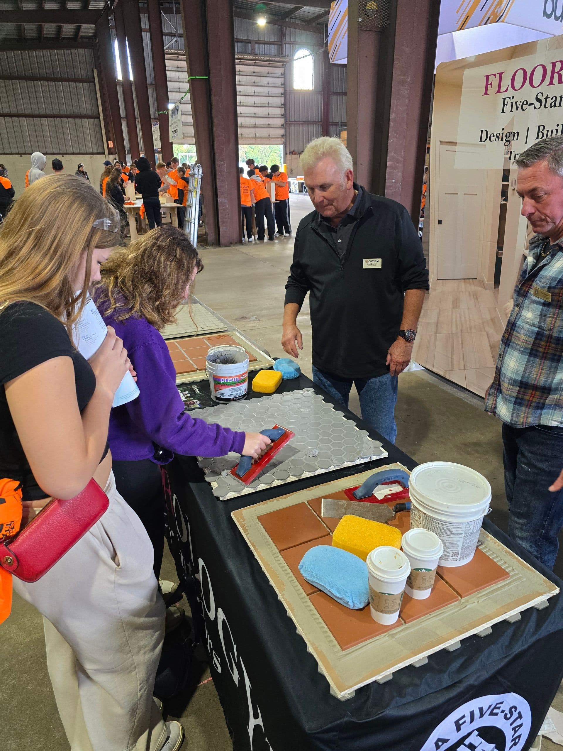 loorology co-founder and Certified Tile Installer Tim Knipper and Fred Zimmer of Custom Building Products guide a student through a hands-on tile activity at Build My Future Northcentral Wisconsin. Photo courtesy of Floorology.