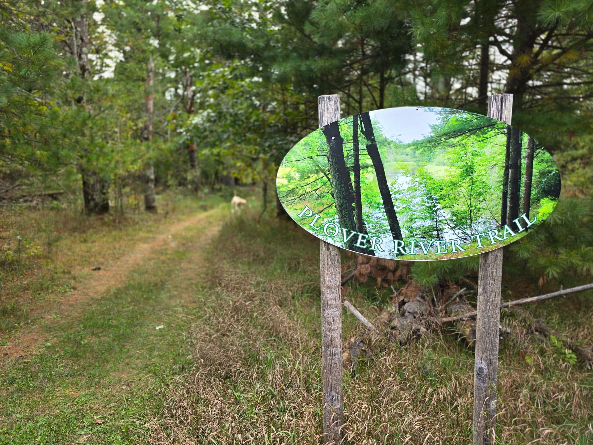 Verde Villa's peaceful riverfront walking trail entrance sign with green trees and grass.