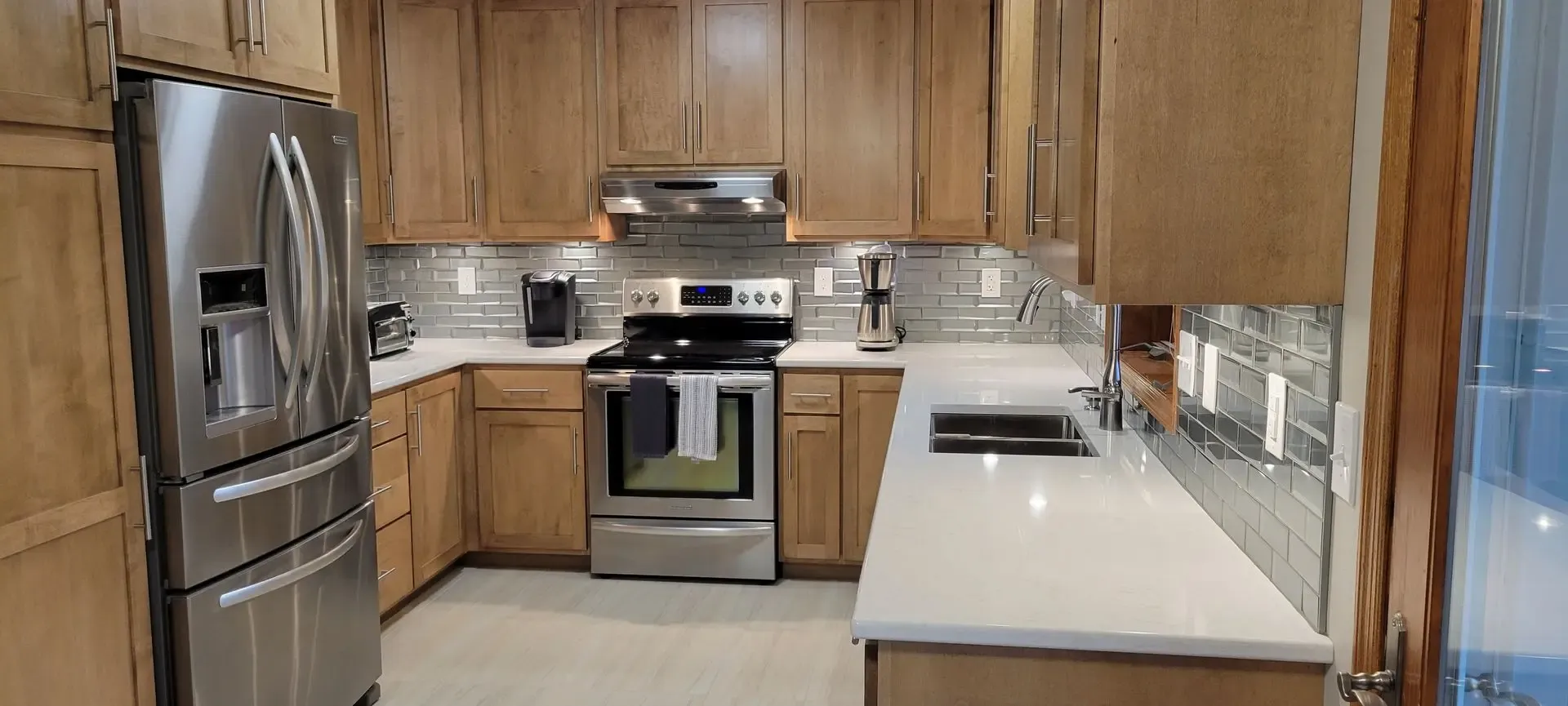 Modern kitchen with wood cabinetry, stainless steel appliances, white quartz countertops, and gray subway tile backsplash