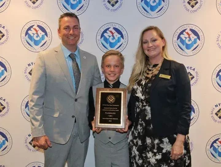 Young boy holding an award plaque standing between two adults at an official event with branded backdrop