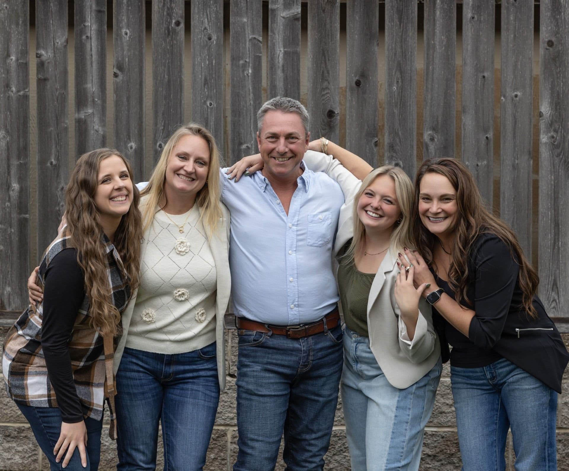 Family of five posing together against a weathered wooden fence, smiling at the camera