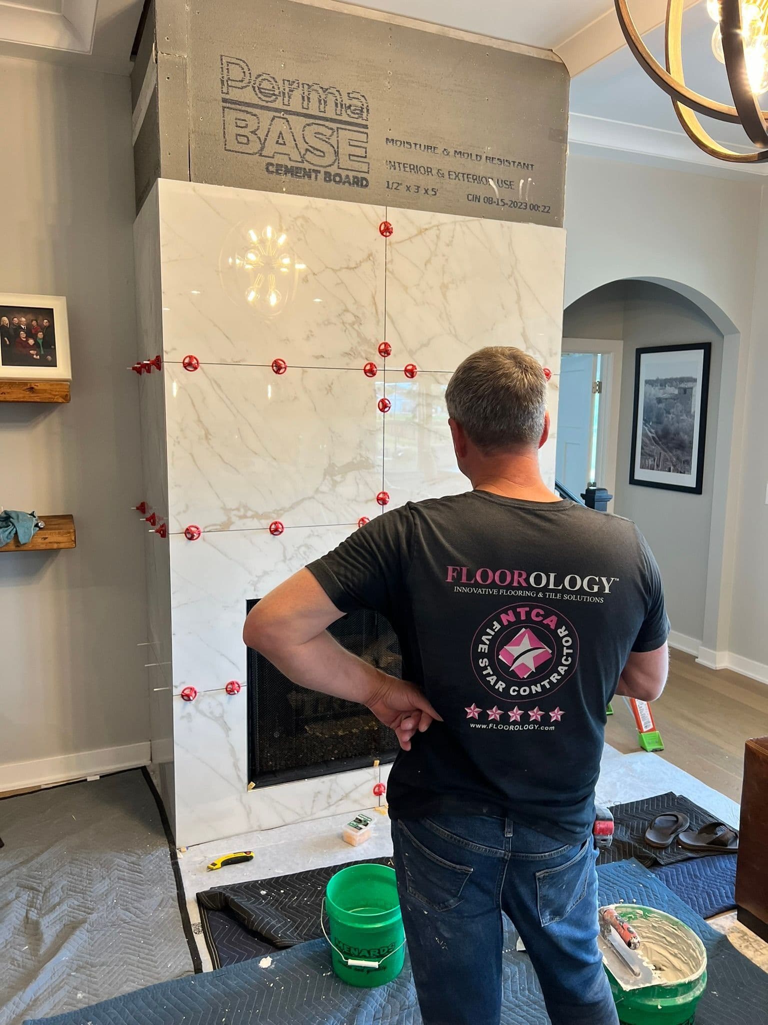 Flooring installer examining Perma BASE cement board sample display with marble-look tiles marked with red measurement guides during installation planning