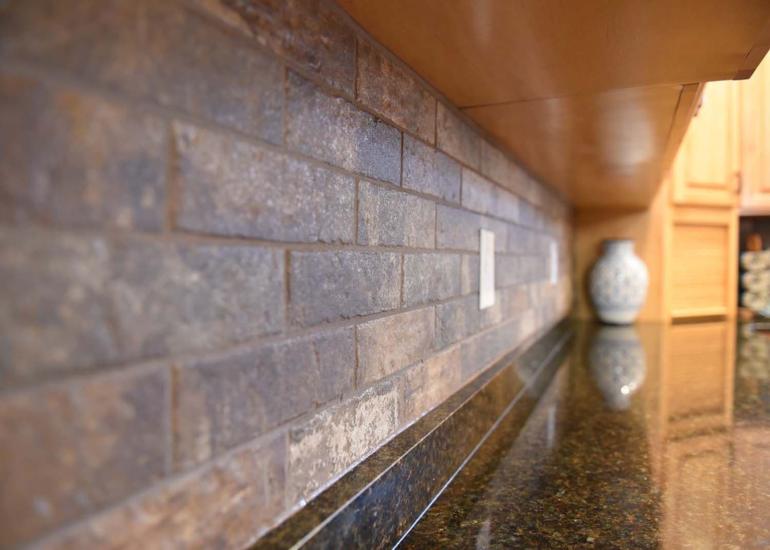 Brown tile backsplash on kitchen countertop with light fixture and decorative vase visible behind