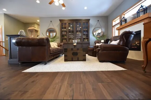 Elegant living room featuring two brown leather Chesterfield sofas facing a wooden coffee table, with built-in cabinetry, pendant lights, and hardwood flooring throughout